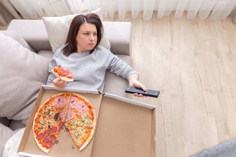 Mujer comiendo pizza en sillón